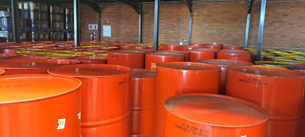 A warehouse filled with rows of large, orange metal barrels under a high ceiling. The brick walls and industrial setting convey a sense of storage and industry.